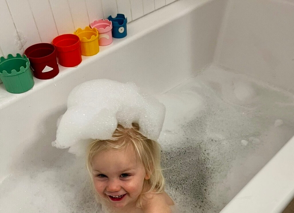 Eczema bath routine for toddlers — Claire smiling in a filtered bubble bath