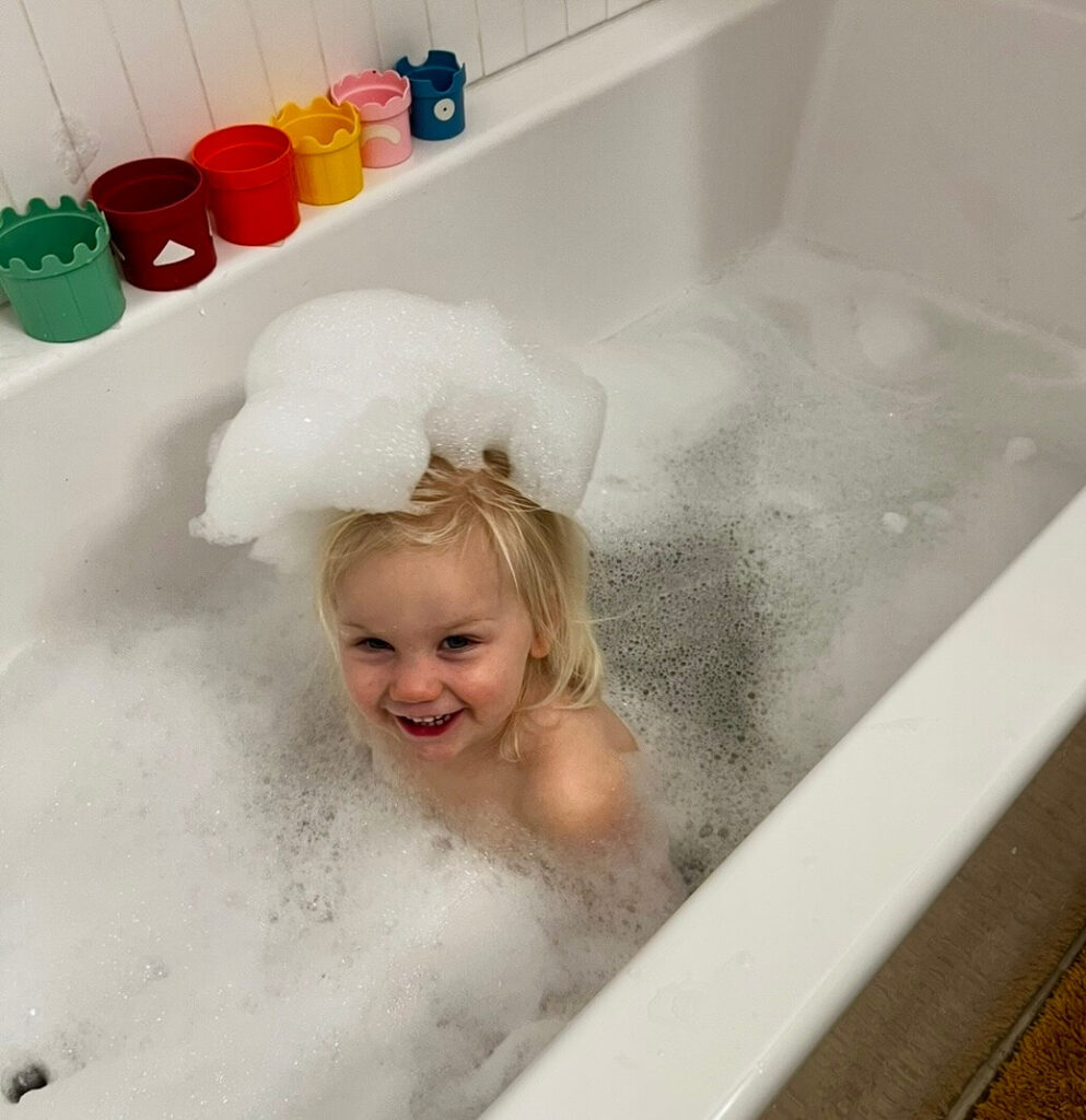 Eczema bath routine for toddlers — Claire smiling in a filtered bubble bath
